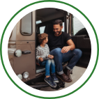 A father and son sit in the open hatch of a jeep parked outdoors. 